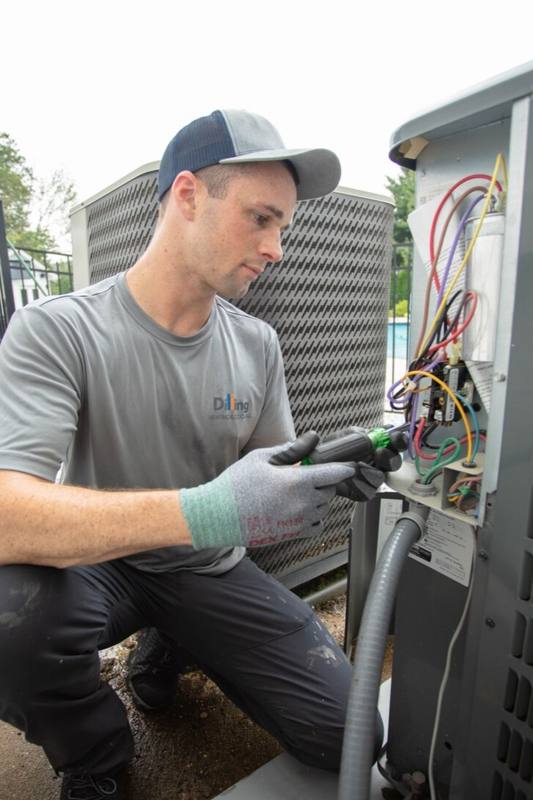 Technician kneeling to test the wiring inside an outdoor condenser unit